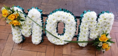 Mom Blue Letter Tribute - White Chrysanthemum with blue ribbon and a variety of yellow and white flowers with mixed foliage.