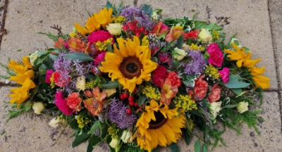 Sunflower Serenity Spray - We create vibrant floral arrangements featuring bright sunflowers blended with soft pink and rich purple blooms, thoughtfully designed to symbolise warmth, love, and remembrance.
