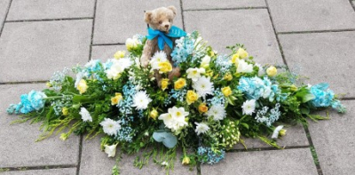Peaceful Skies Spray - A graceful funeral spray of blue, white, and yellow blooms, thoughtfully arranged to symbolise peace, remembrance, and comfort.